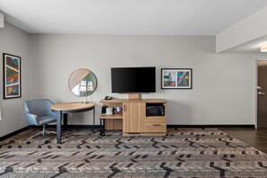 A hotel room with a round table, a blue chair, a flat-screen TV, a microwave, a coffee maker, and a patterned rug. - Hampton Inn & Suites Pauls Valley (Pauls Valley)