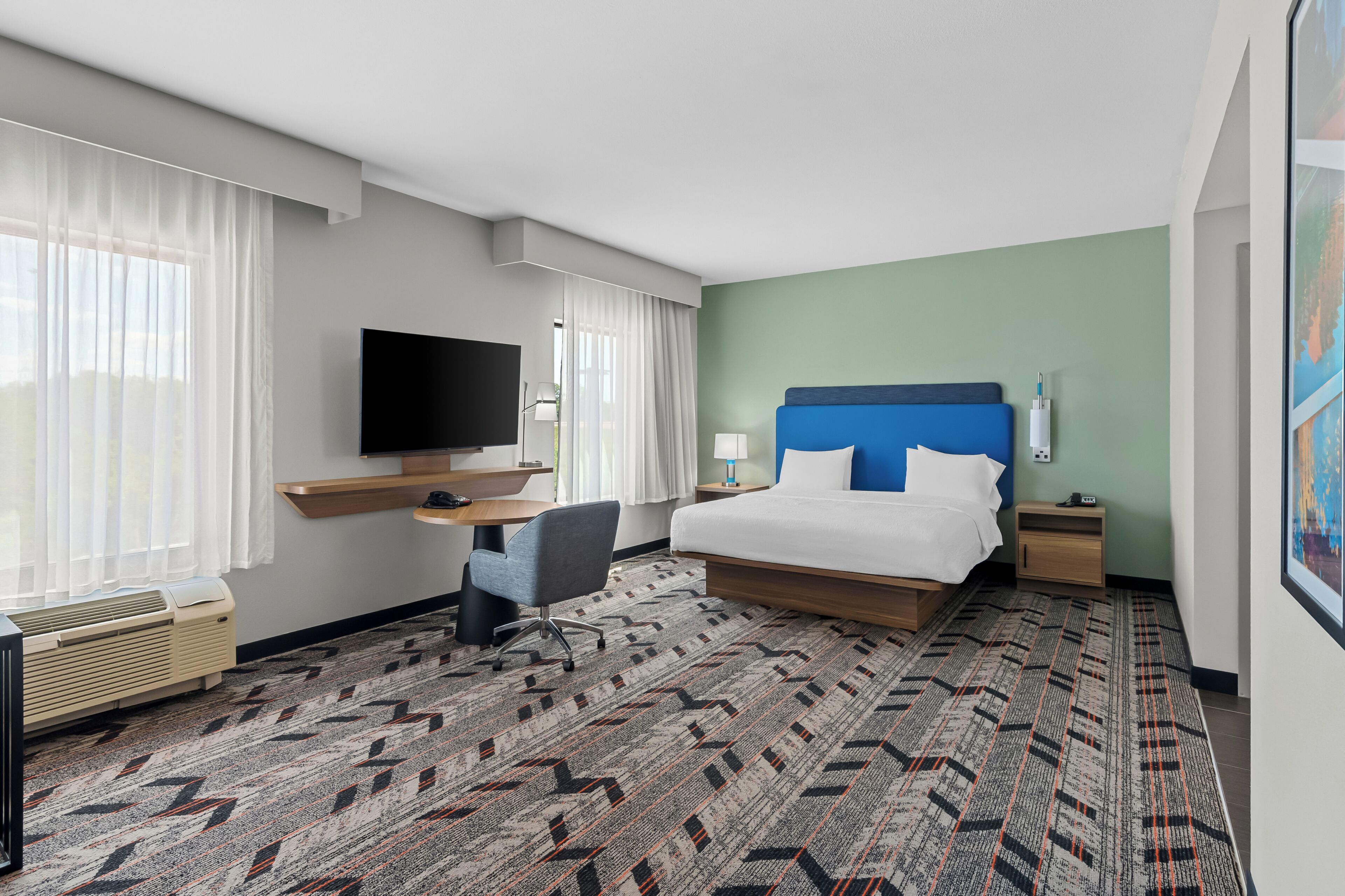A hotel room with a bed, a desk, a chair, a TV, and a large window with curtains.