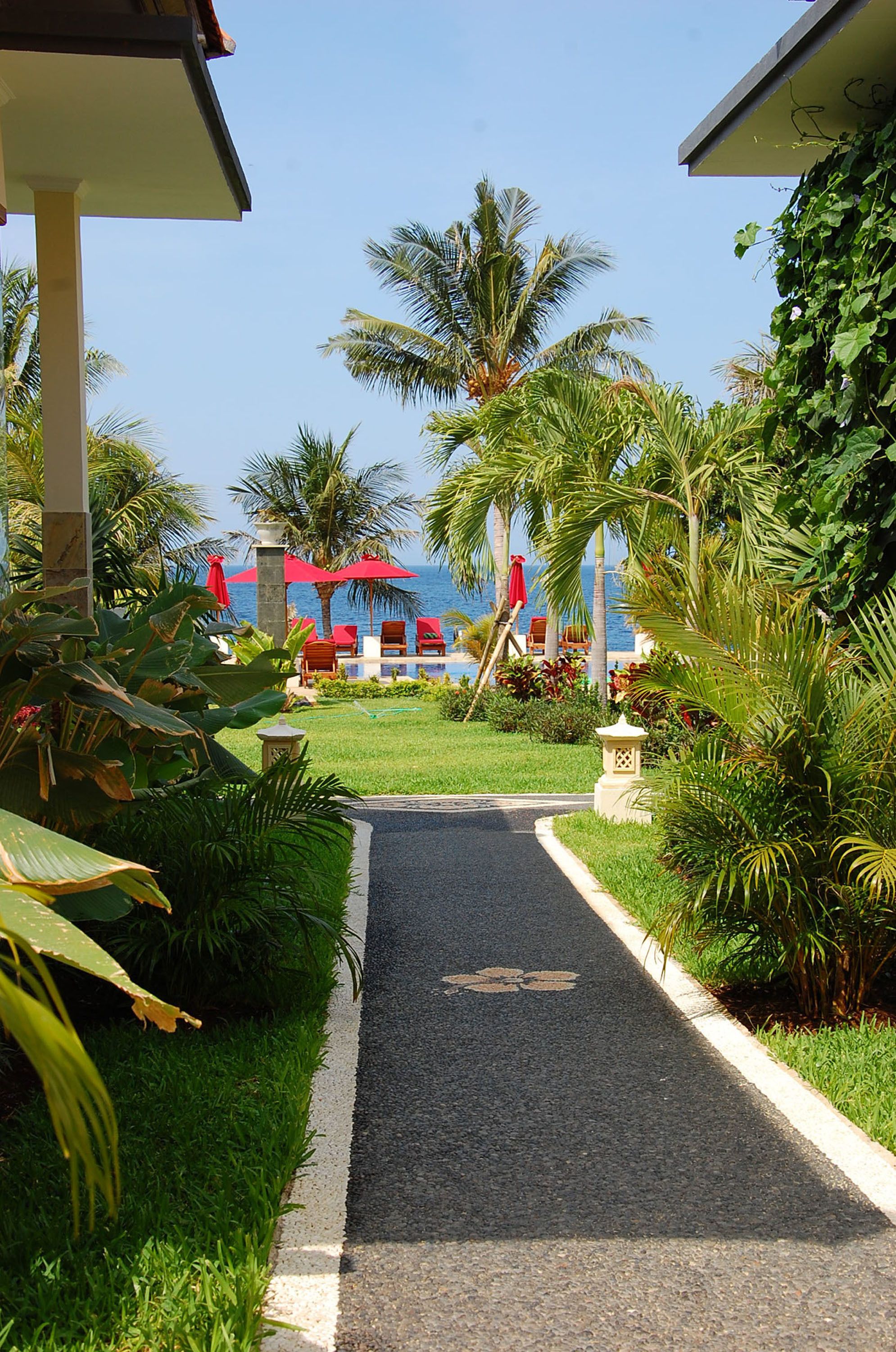 A pathway leading to a beach area with red umbrellas and lounge chairs.