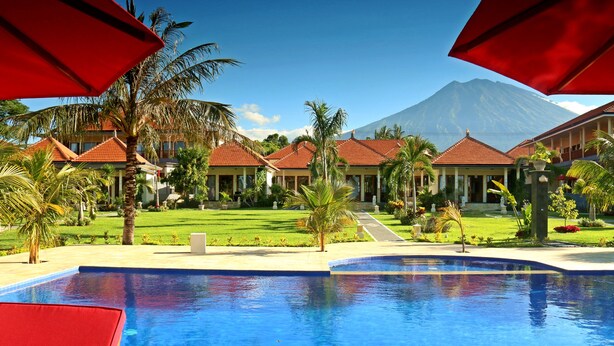 A resort with a swimming pool, palm trees, and a mountain in the background. - Bali Dive Resort and Spa (Tulamben)