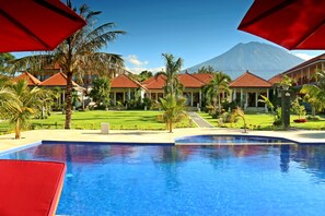 A resort with a swimming pool, palm trees, and a mountain in the background. - Bali Dive Resort and Spa (Tulamben)