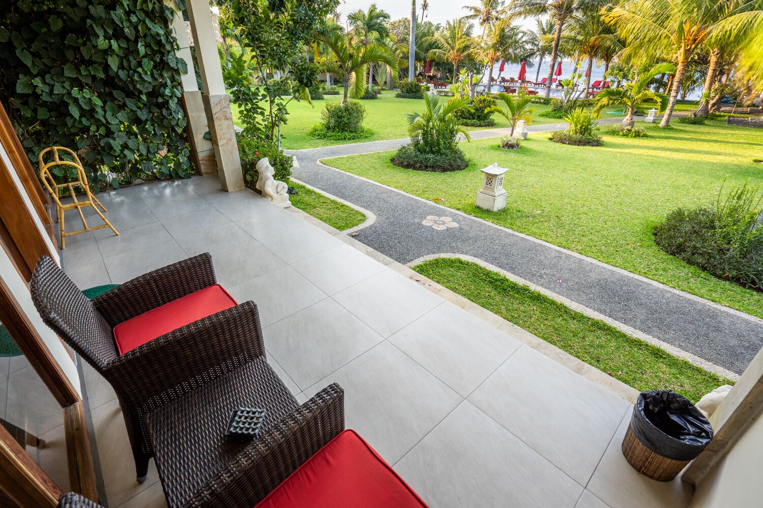 A patio area with wicker furniture and a view of a well-maintained garden and beach.