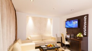 A modern living room with a sofa, a coffee table with fruit, a TV, and a desk with a flower arrangement. - Hôtel Samarons (Ariana)