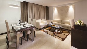 A modern living room with a dining area, featuring a sofa, a coffee table, and a dining table set for four. - Hôtel Samarons (Ariana)