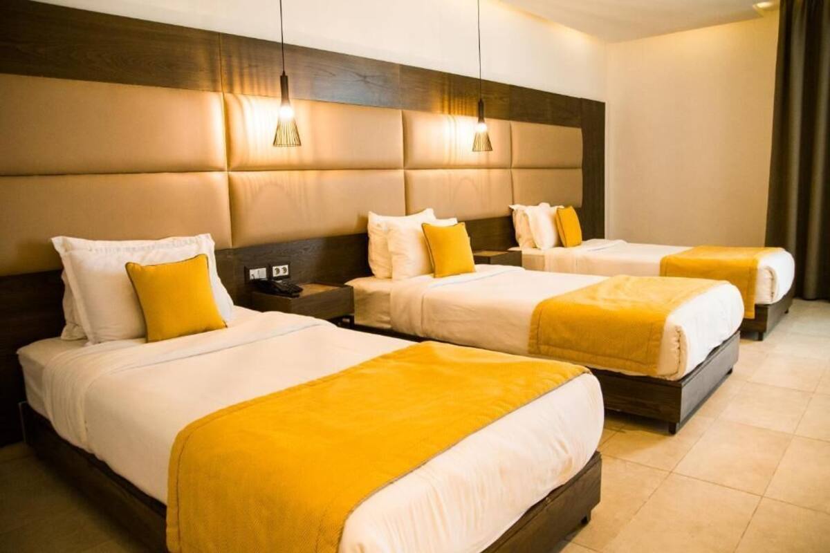 A hotel room with three beds, each with white bedding and yellow accents.