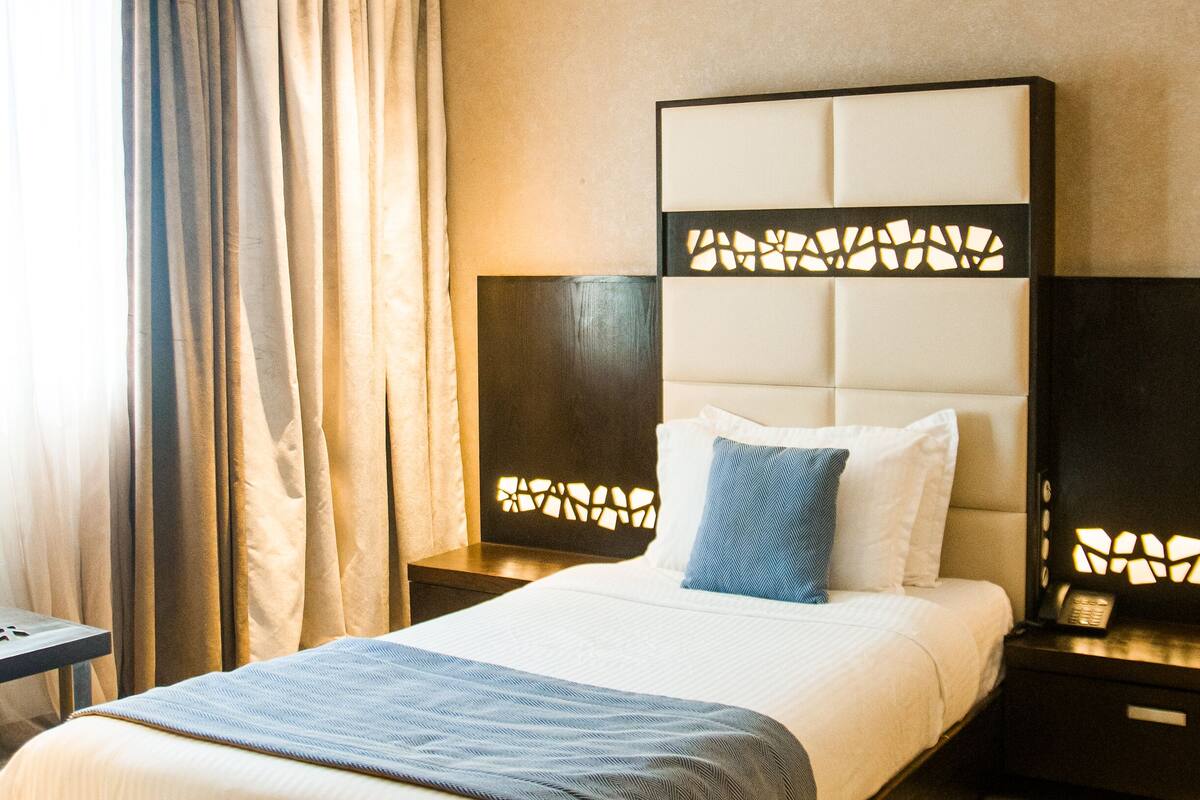 A hotel room with a large bed, a headboard with a geometric pattern, two bedside tables with lamps, and a patterned floor.