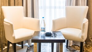 Two white armchairs facing each other with a small table between them, a bottle, and a lighter on the table. The room has a marble floor and beige curtains. - Hôtel Samarons (Ariana)