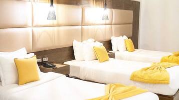 A hotel room with three beds, each with white bedding and yellow accents. There are bedside tables with lamps and a phone on one of them.