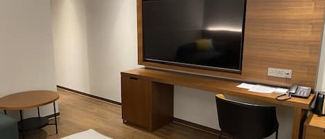 Una habitación de hotel con un escritorio de madera, un televisor de pantalla plana, un teléfono y una mesita redonda.