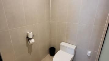 Un baño pequeño con azulejos, un inodoro, un cubo de basura y un dispensador de papel higiénico.