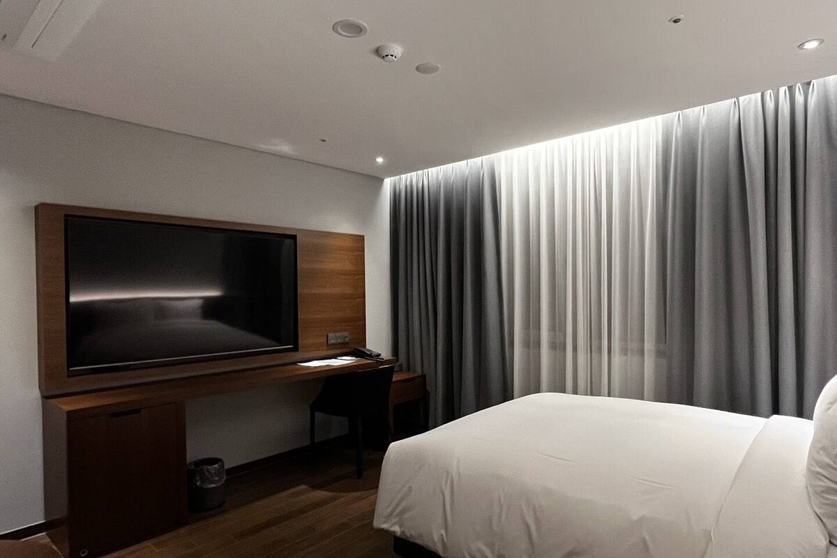 Une chambre d’hôtel avec un lit, un bureau avec une télévision et une grande fenêtre avec des rideaux.