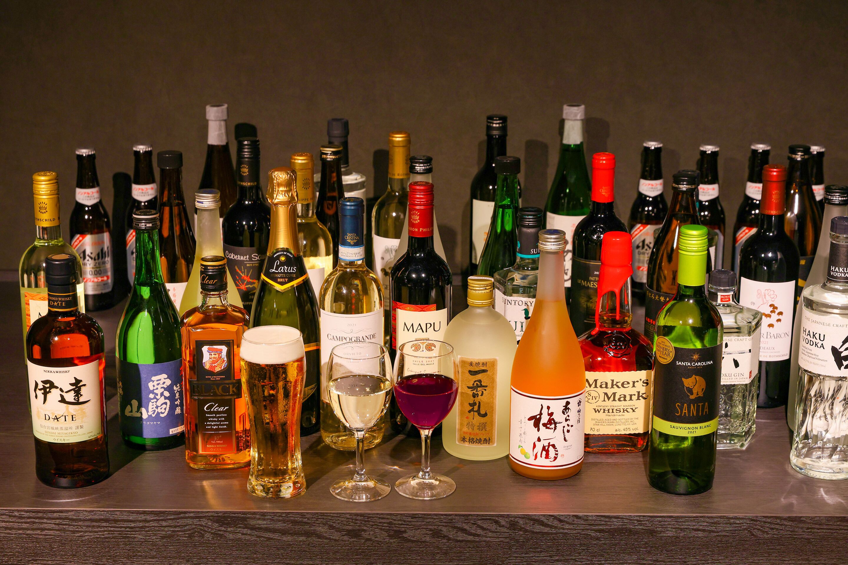 Variedad de botellas y vasos con bebidas alcohólicas en una estantería.