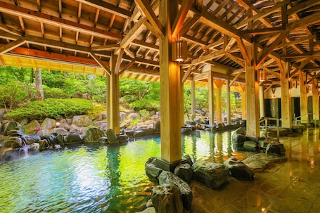 A traditional wooden structure with a stone water feature and a view of lush greenery outside.