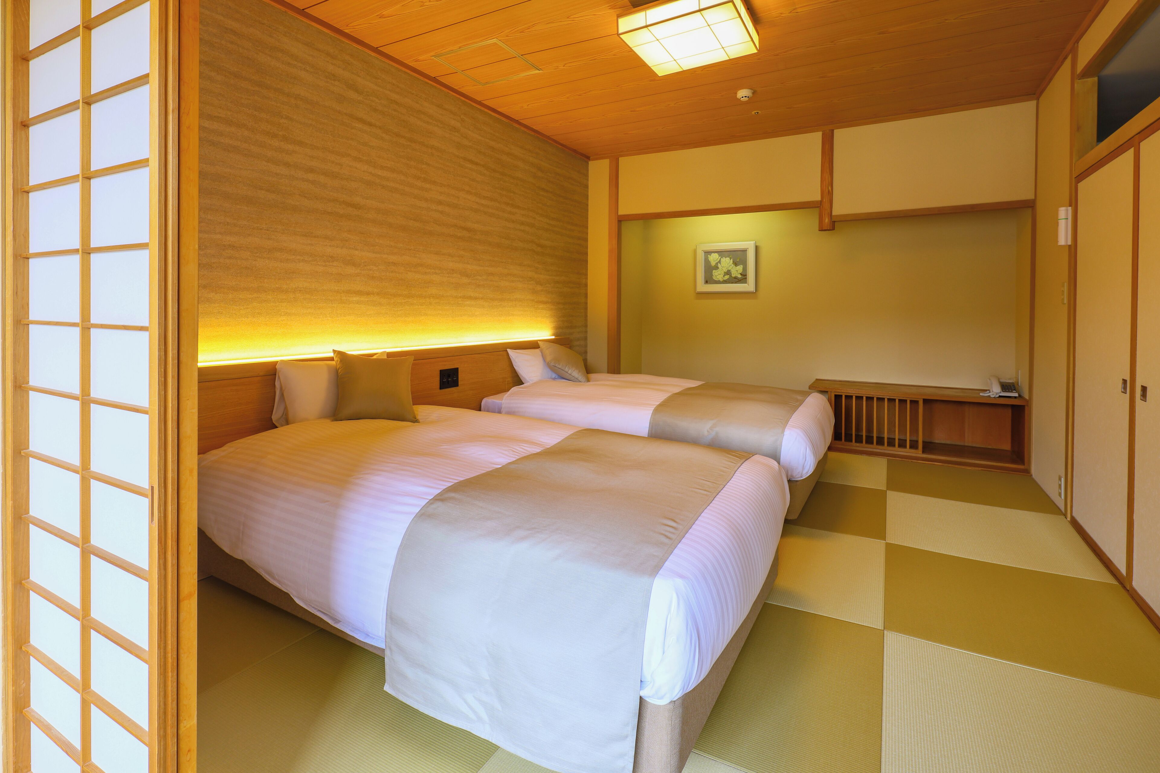 A traditional Japanese-style room with tatami flooring, two beds with white bedding, a wooden ceiling with a light fixture, and a shoji screen.