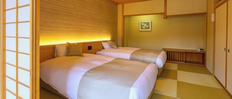 A traditional Japanese-style room with tatami flooring, two beds with white bedding, a wooden ceiling with a light fixture, and a shoji screen.