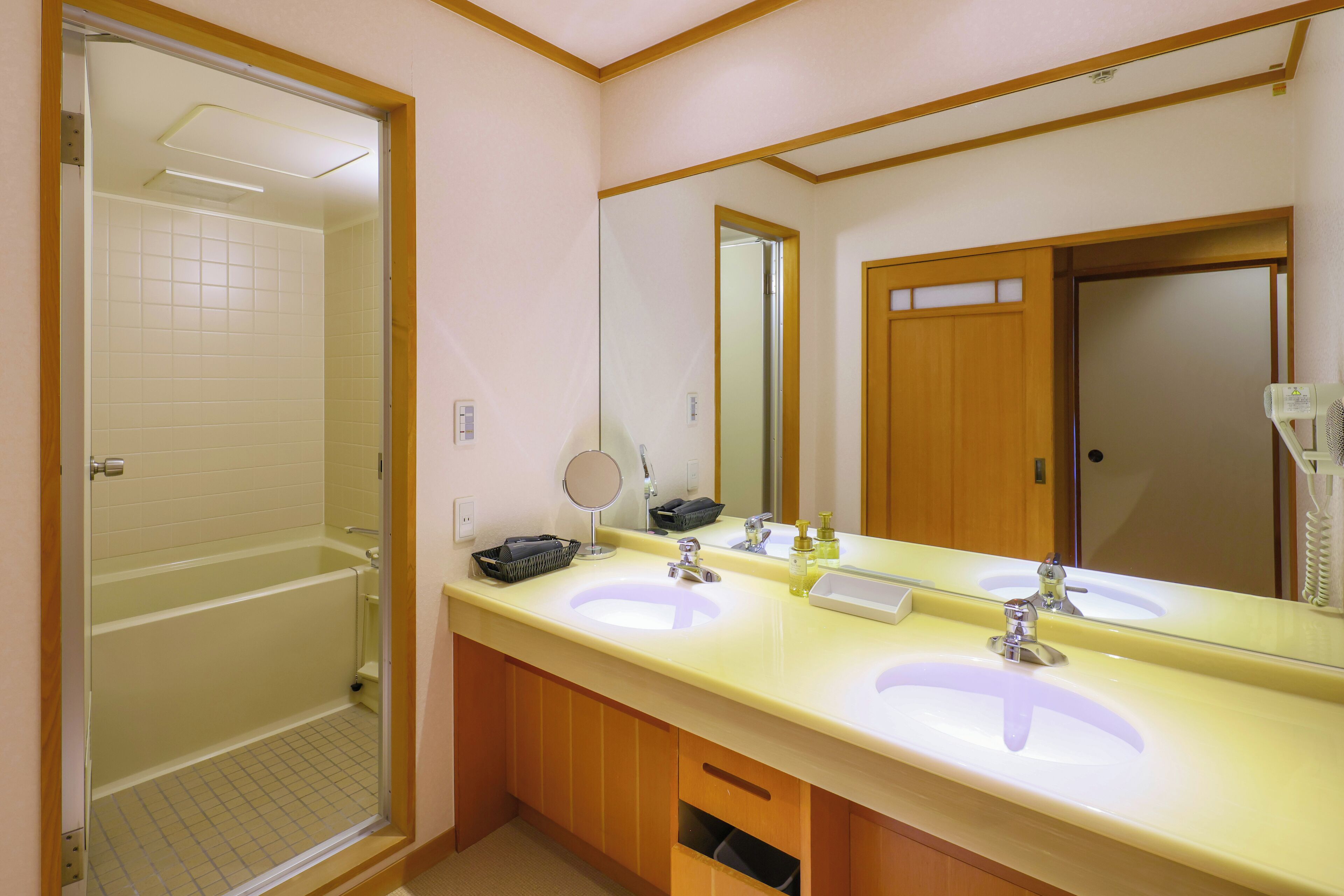 A bathroom with two sinks, a mirror, a shower, and a wooden door.