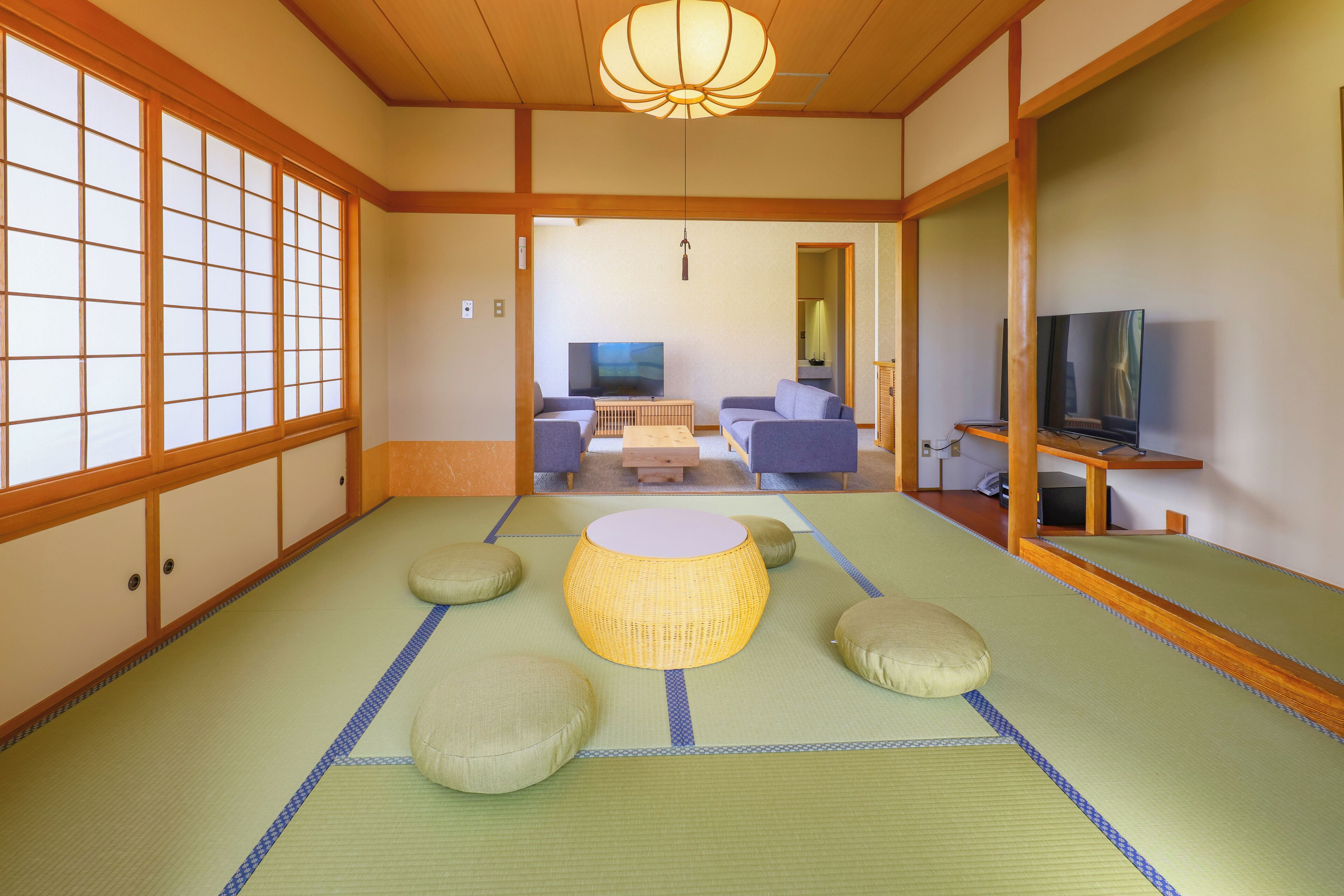 Une pièce de style japonais traditionnel, avec un sol recouvert de tatamis, une table basse, des coussins et un téléviseur.