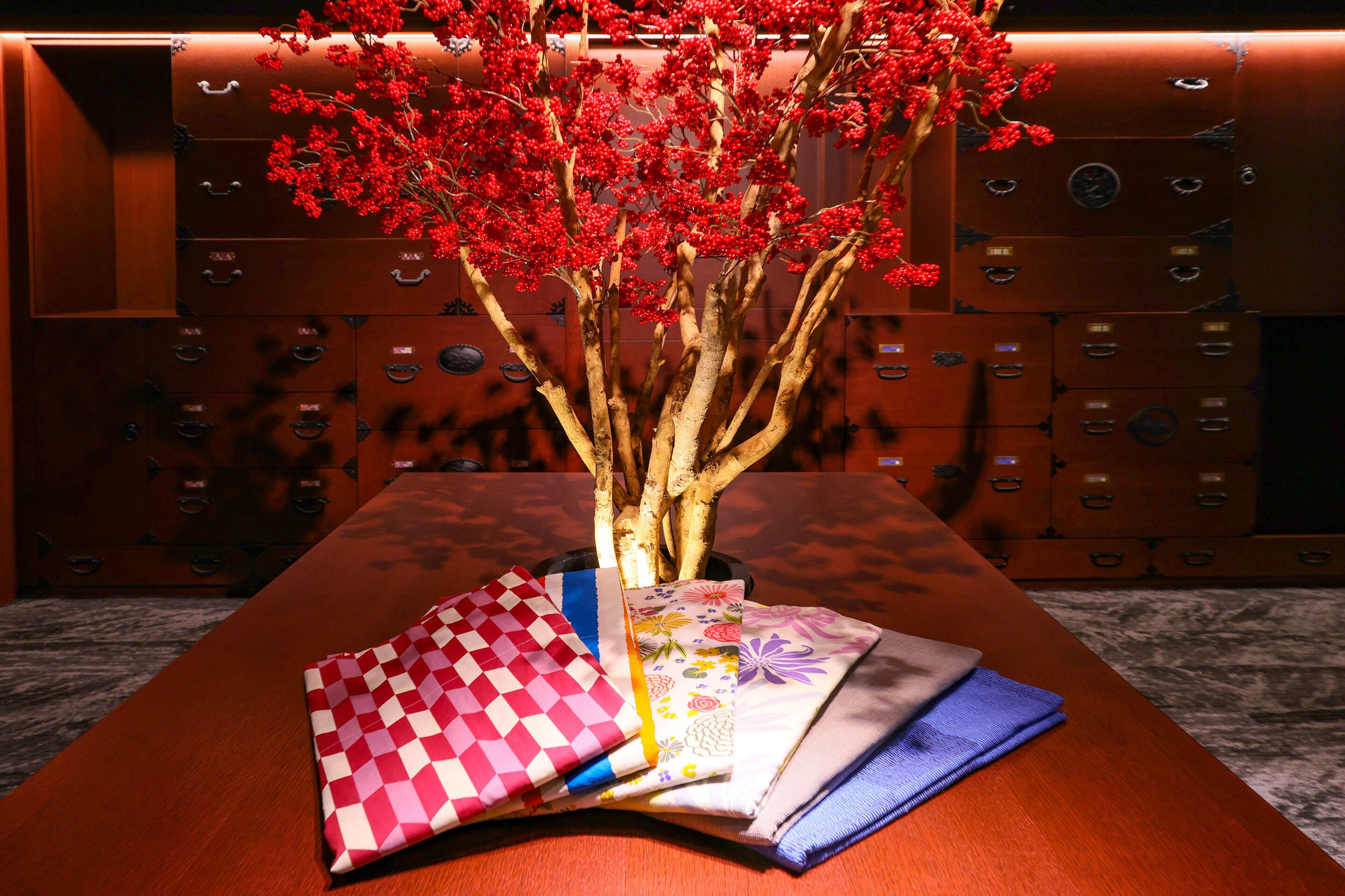 Una mesa de madera con un jarrón de flores rojas y telas dobladas.