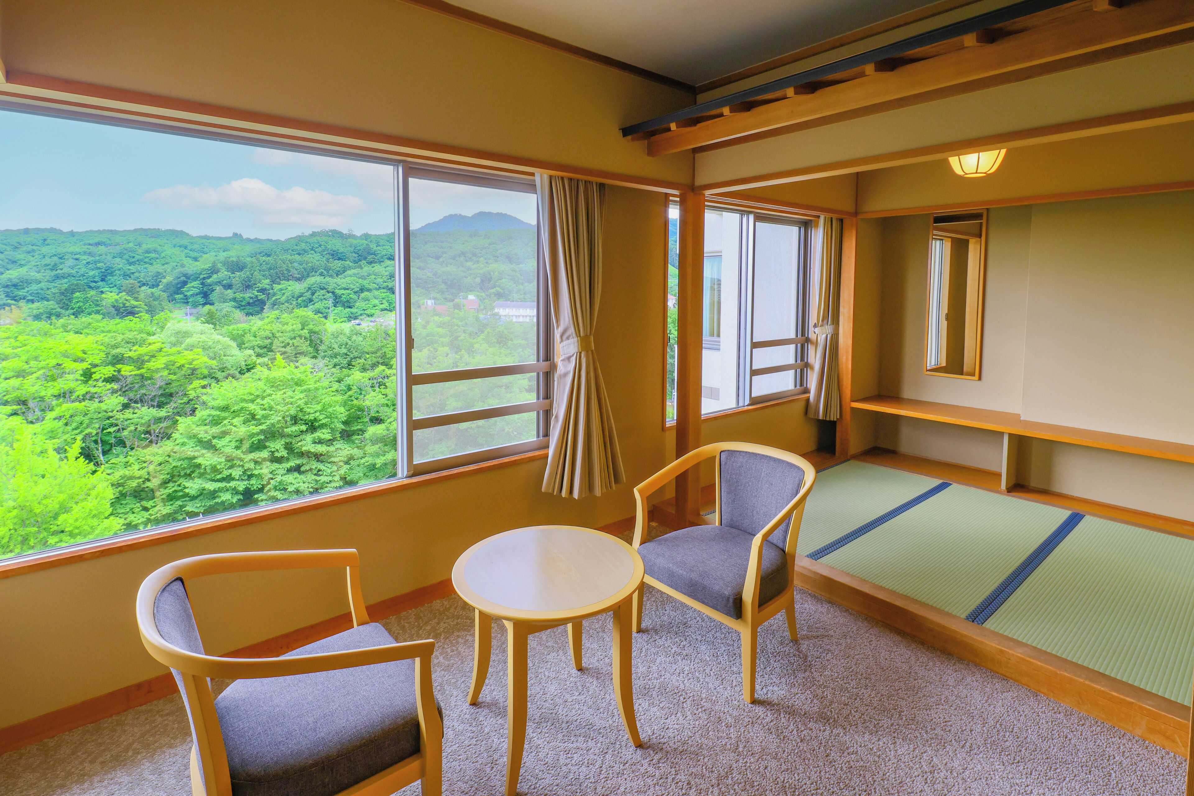 A room with a view of a forest, a tatami mat, and a traditional Japanese-style table and chairs.