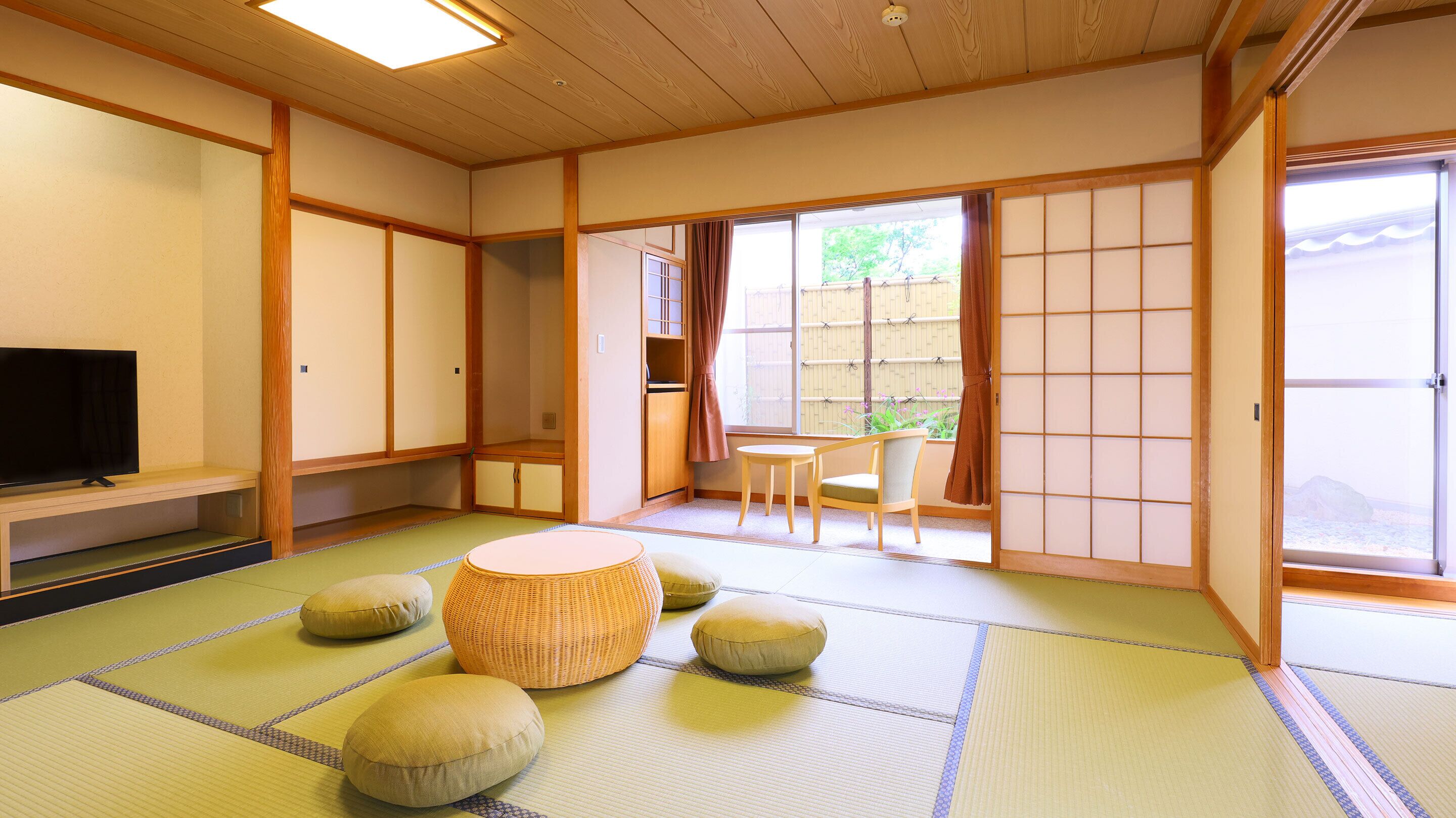 A traditional Japanese room with tatami flooring, a television, a low table with cushions, and sliding doors leading to a balcony.