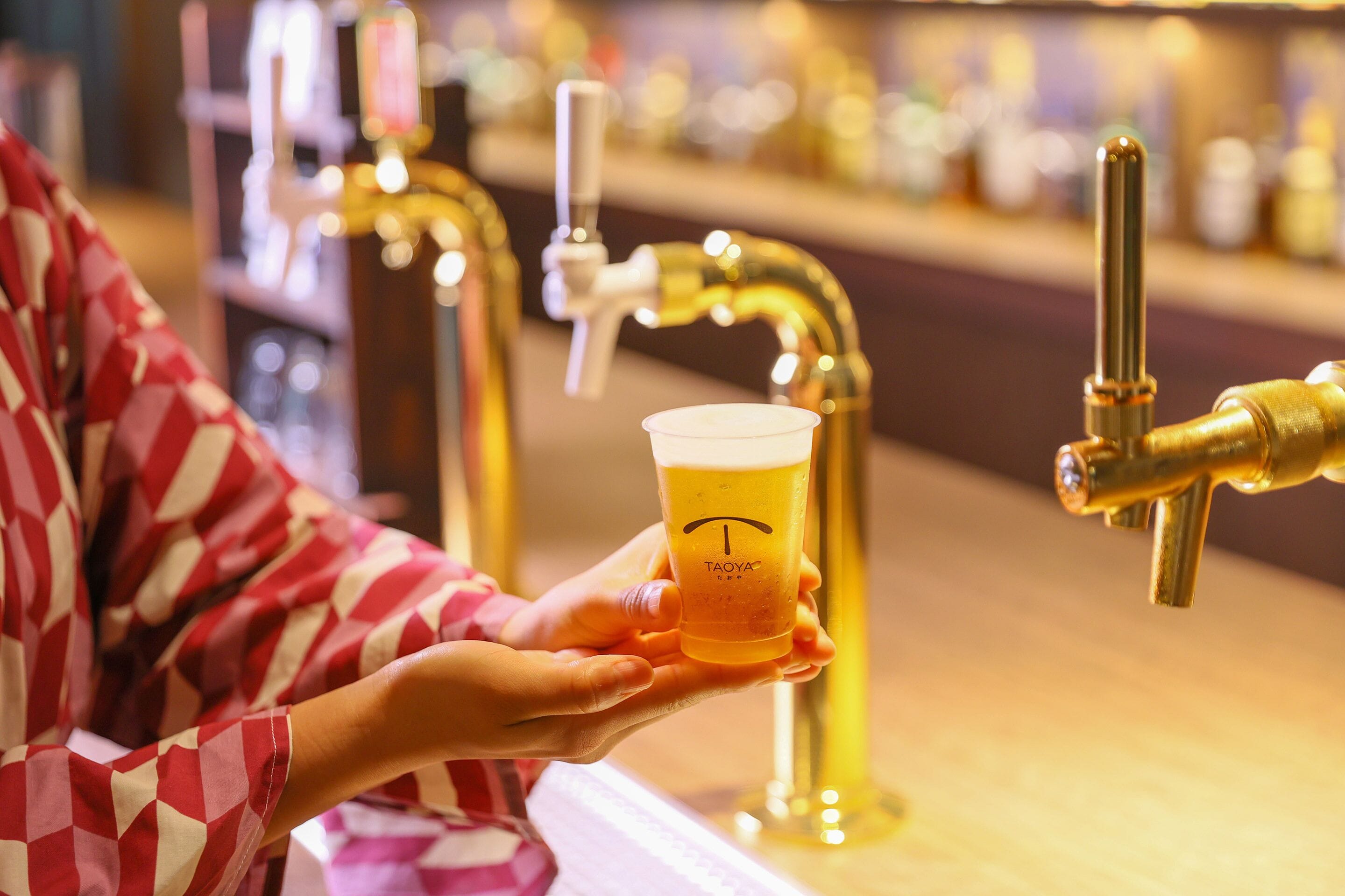 Une personne tenant un verre de bière dans un bar où l’on propose plusieurs sortes de bières à la pression.
