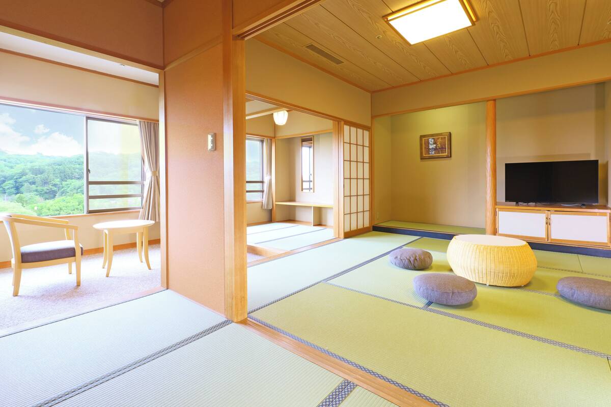 Une pièce de style japonais traditionnel, avec un sol recouvert de tatamis, un téléviseur et une vue sur l’extérieur.