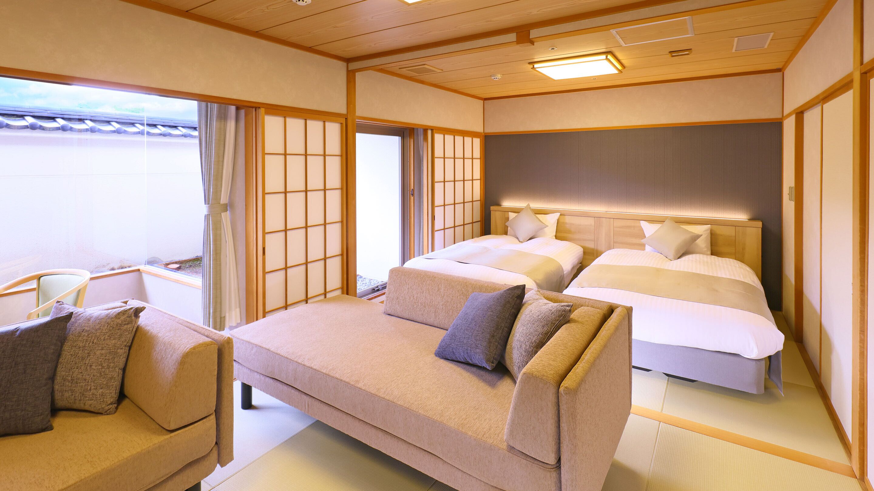 Ein traditionell eingerichtetes Hotelzimmer im japanischen Stil mit Tatami-Böden, einer niedrigen Plattform-Liege, einer Couch und verschiebbaren Shoji-Türen.