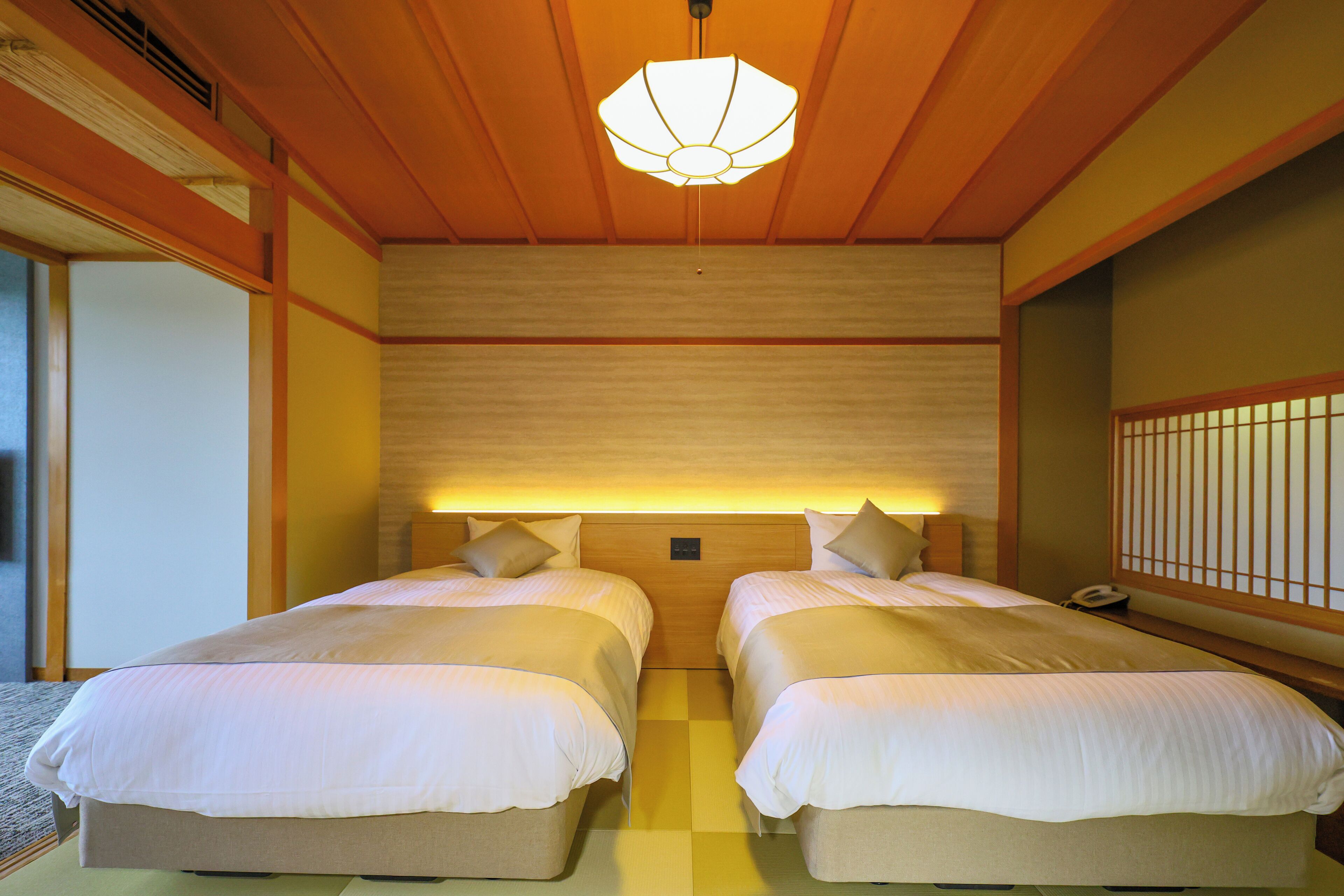 Une chambre d’hôtel avec deux lits, des lambris en bois, un luminaire de plafond de style japonais traditionnel et un téléphone sur la table de chevet.