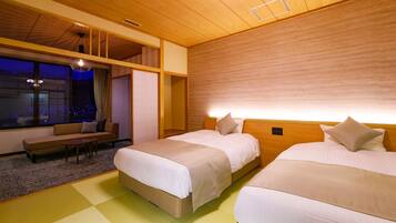 A hotel room with two beds, a sofa, a small table, and a large window with a view of the city at night.
