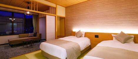 A hotel room with two beds, a sofa, a small table, and a large window with a view of the city at night.