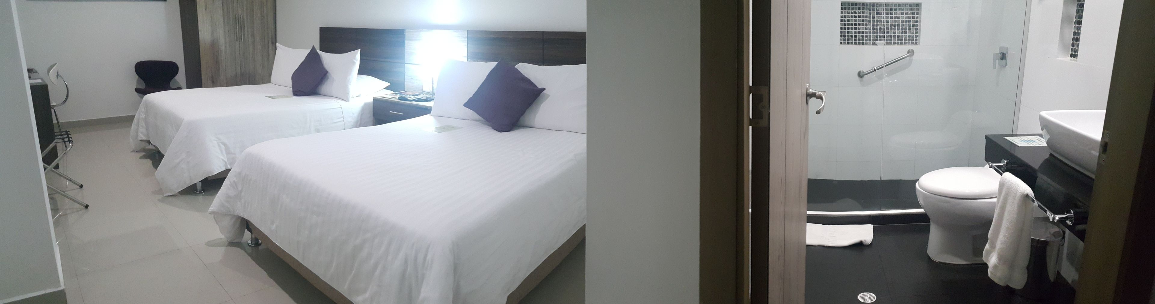 Habitación de hotel con dos camas, baño con inodoro, lavamanos y ducha.