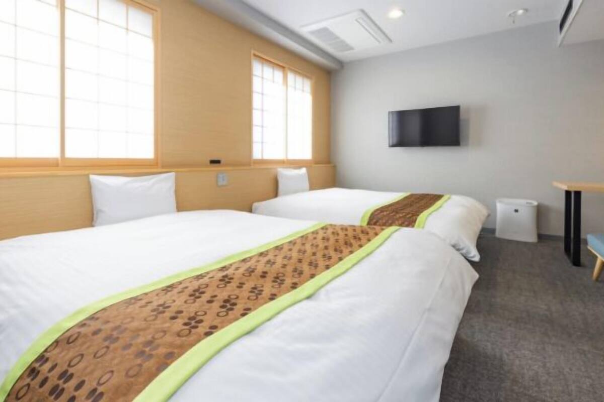 A hotel room with two beds, a TV on the wall, and a desk.