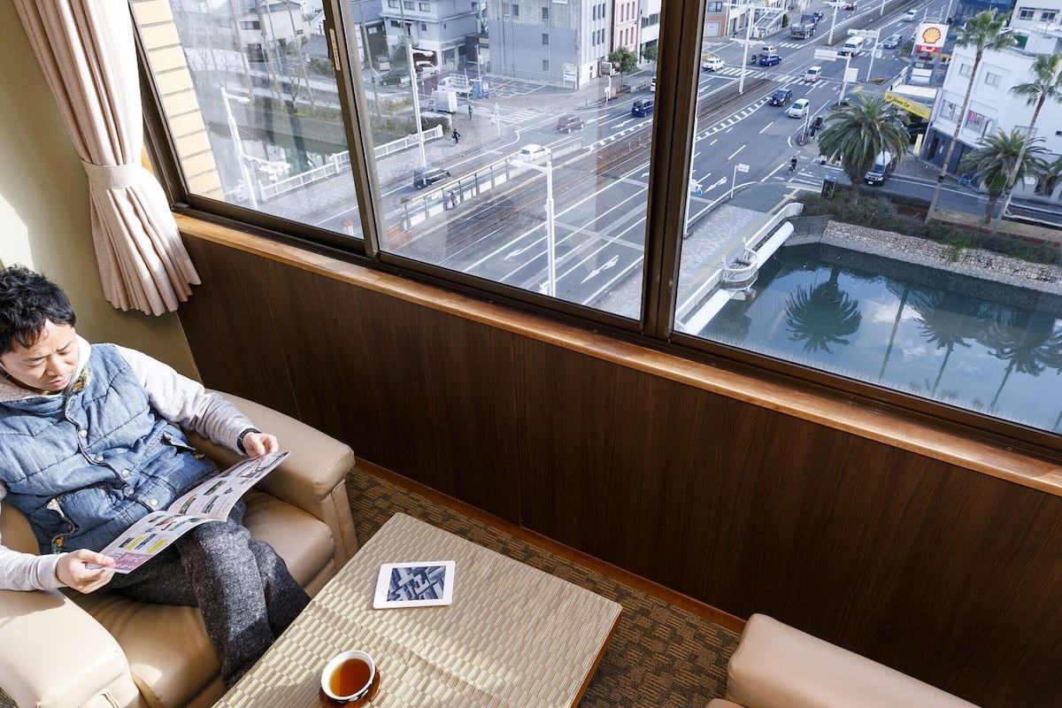 A person sitting on a sofa in a room with a large window overlooking a cityscape.
