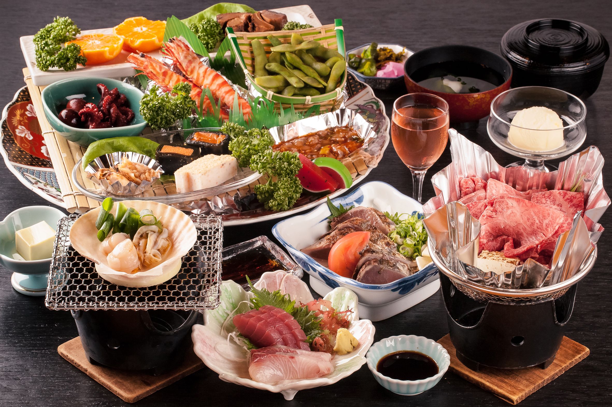 Variedad de sushi y sashimi, una olla caliente y una copa de vino sobre una mesa de madera.