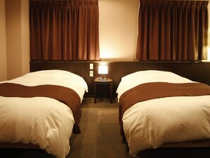 A hotel room with two beds, a nightstand with a lamp, and brown curtains. - Hotel Takasago (Kochi)