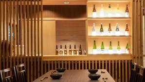 A restaurant interior with a wooden slatted wall, a central table with two chairs, and shelves displaying various bottles. - Hotel Takasago (Kochi)