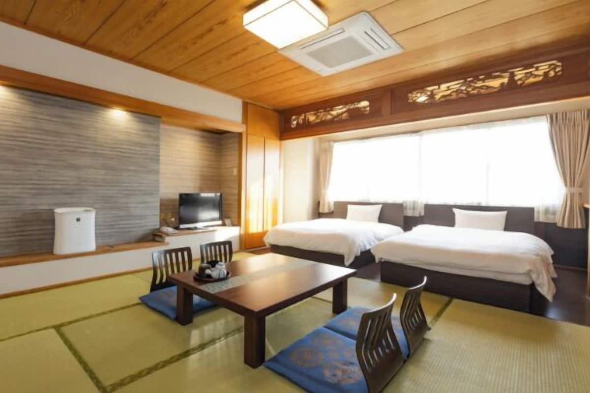 A hotel room with two beds, a television, a small table, and a traditional Japanese tatami mat floor.