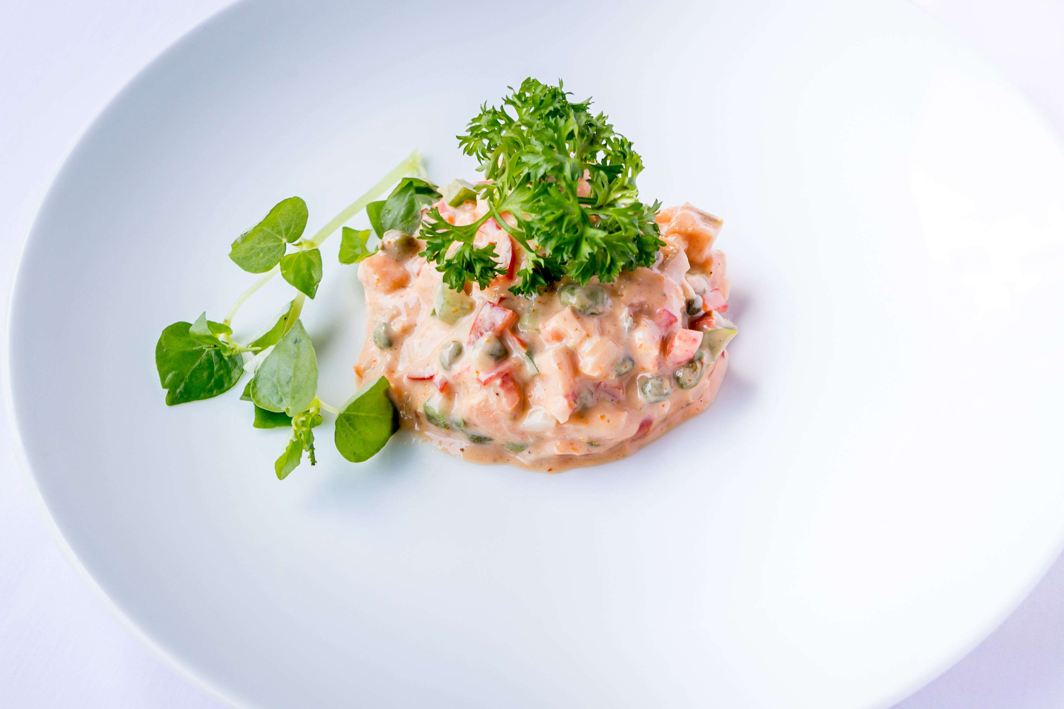 A dish with a creamy base, green herbs, and red pieces, served on a white plate.