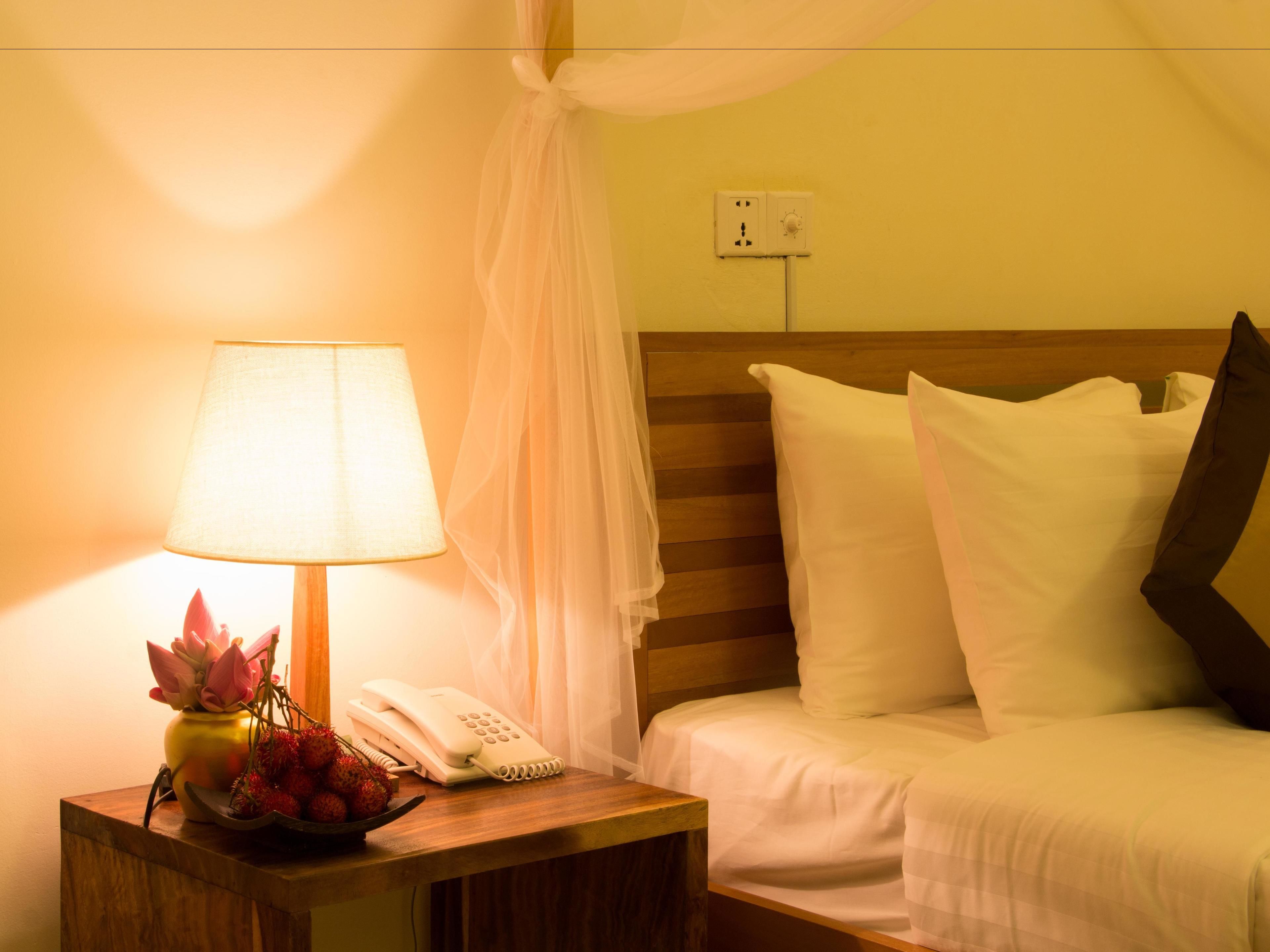 Una habitación de hotel con una mesita de noche que incluye una lámpara, un florero con flores y un teléfono.