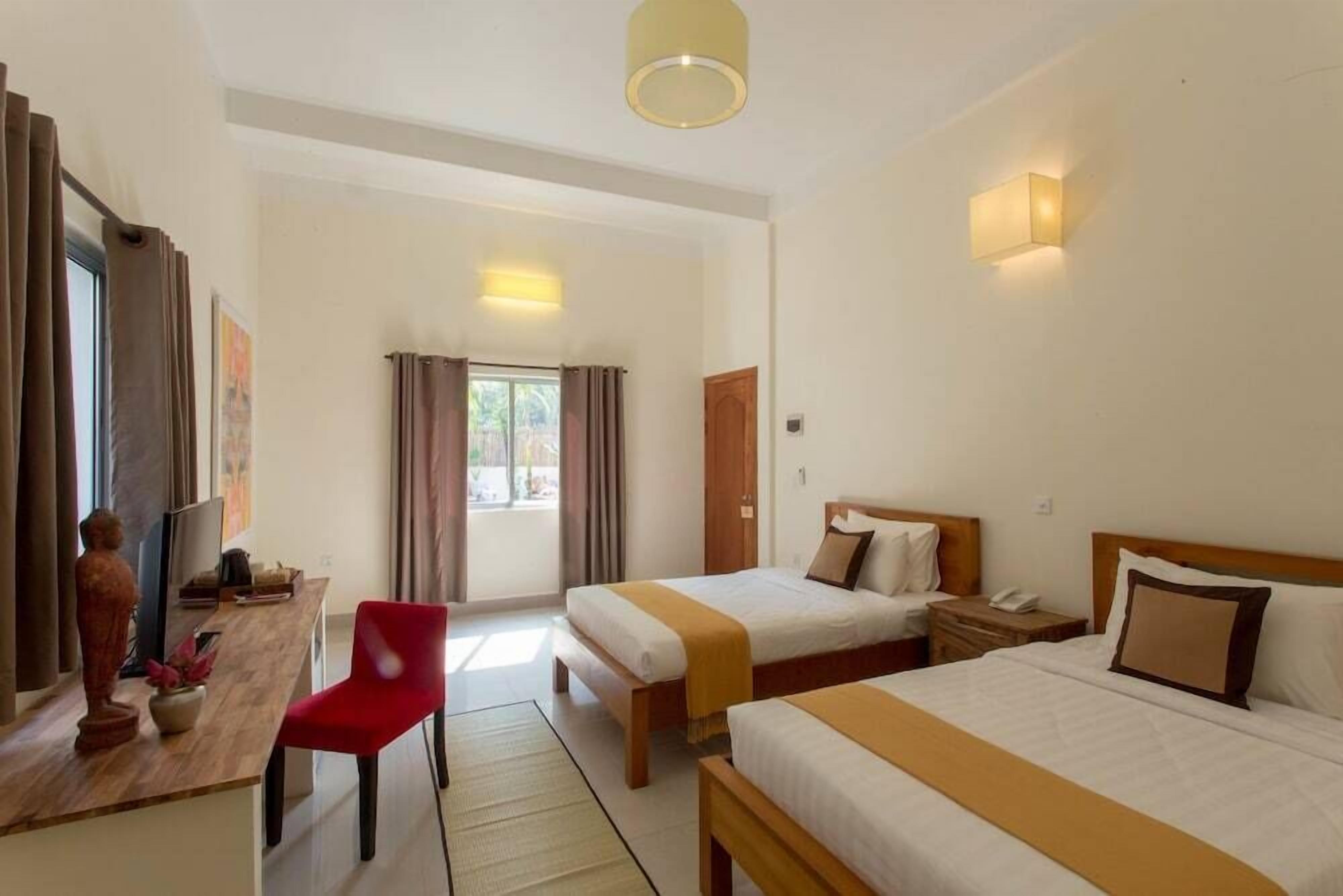 A hotel room with two beds, a desk, a chair, and a television.