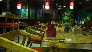 A restaurant with wooden chairs and red cushions, a table set with glasses and cutlery, and red hanging lamps. - River and Villa (Siem Reap)