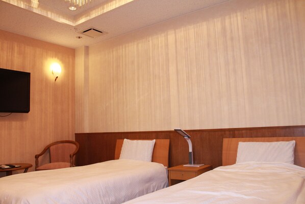 A hotel room with two beds, a wooden headboard, a nightstand with a lamp, a chair, and a TV mounted on the wall. - Honjin Sakura-tei (Yuzawa)