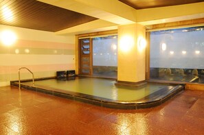 A heated indoor pool area with a tiled floor, a metal ladder, and a glass partition. - Honjin Sakura-tei (Yuzawa)