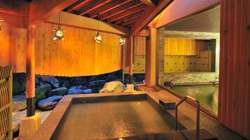 A hot tub area with wooden walls, a stone border, and a view of a pool.