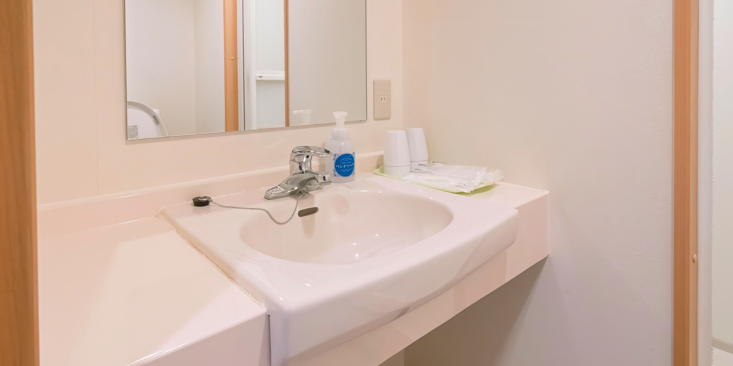 A bathroom with a white sink, a mirror, and a faucet. There are two bottles of hand soap and a cup on the counter.