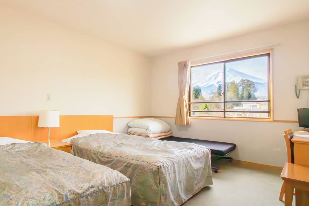 A hotel room with two beds, a desk, a chair, a lamp, and a window with a mountain view.