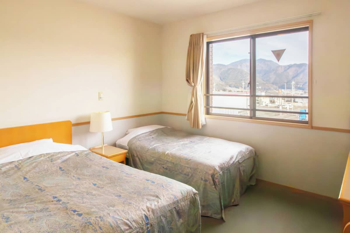 A hotel room with two beds, a nightstand, a lamp, a window with a view of mountains, and a desk with a telephone.