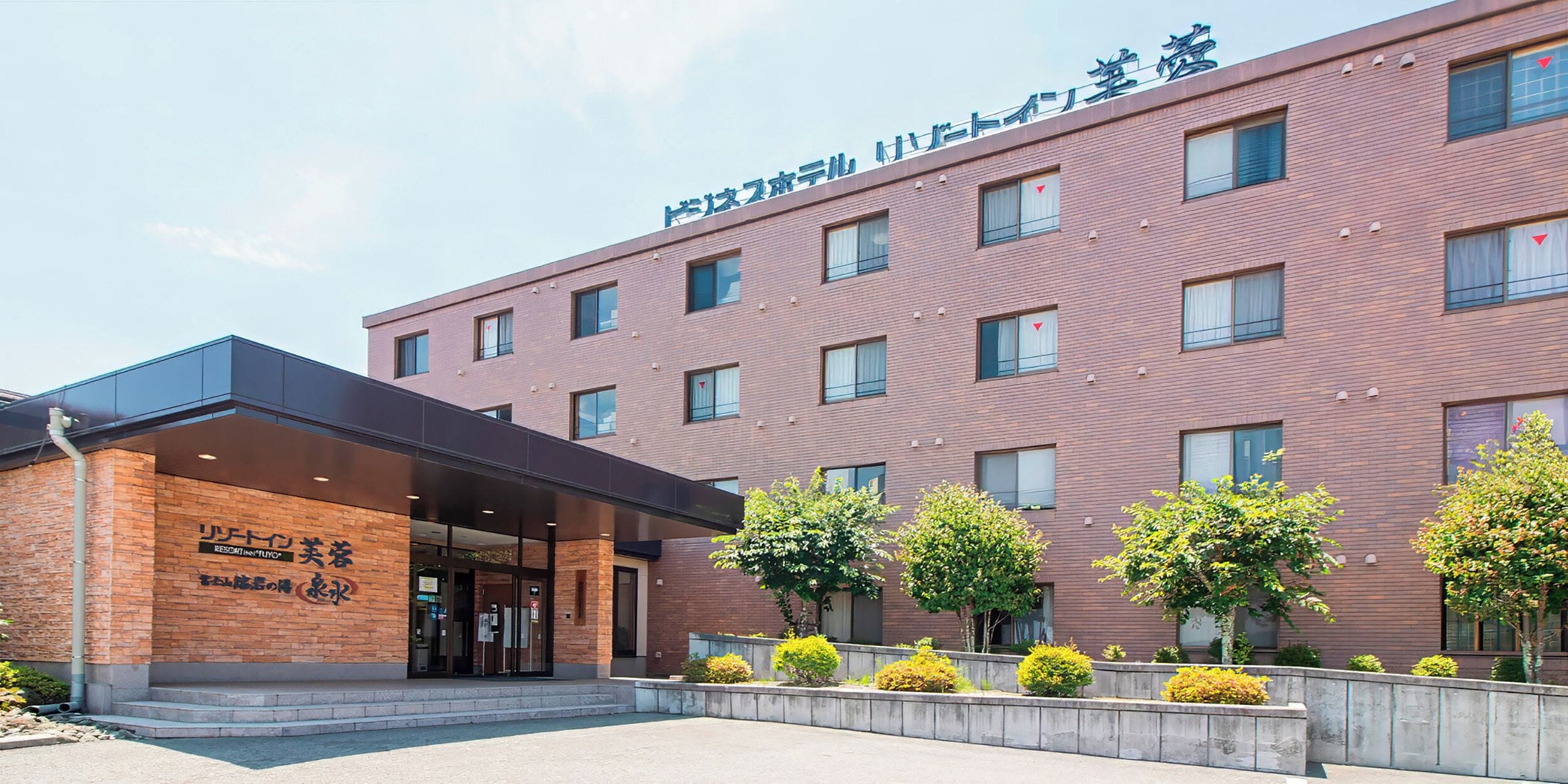 A multi-story hotel with a brick facade, a covered entrance, and a landscaped area with trees.