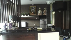A modern kitchen with a dark wood countertop, a refrigerator with magnets, a small potted plant, and a painting on the wall. - Griya Nendra Hotel (Ngaglik)
