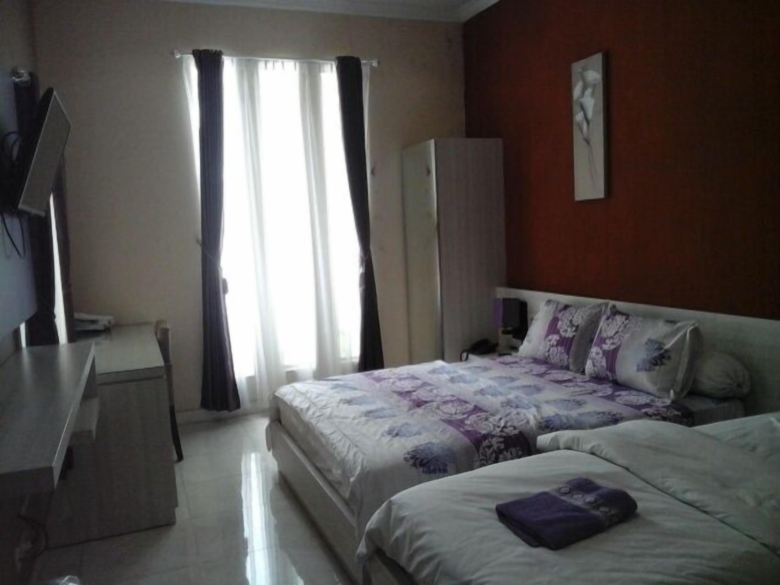 Una habitación de hotel con cama, escritorio, armario y ventana con cortinas.